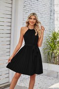 Woman wearing a black halter neck chiffon sundress with a pleated skirt and an adjustable waist tie.