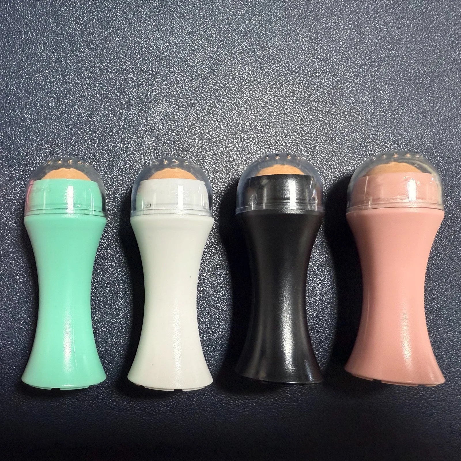 Portable volcanic stone facial roller for oily skin control in black, green, pink, or white.