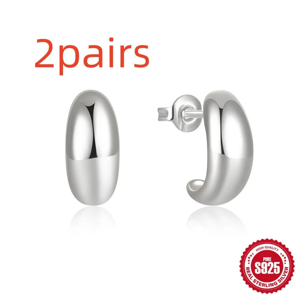 Close-up of a glossy C-shaped sterling silver stud earring in gold electroplated finish on a plain background.