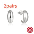 Close-up of a glossy C-shaped sterling silver stud earring in gold electroplated finish on a plain background.