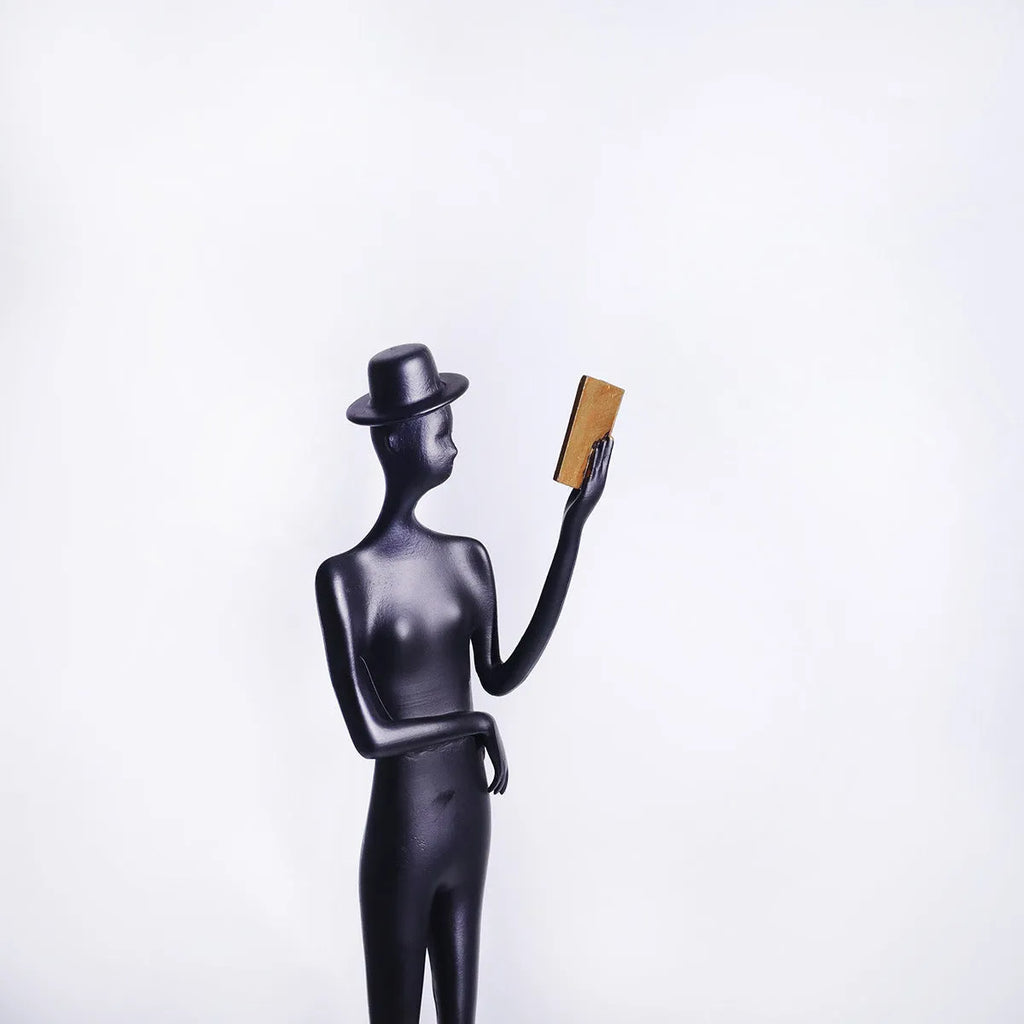 Black cast aluminium sculpture of a woman reading, modern minimalist style.