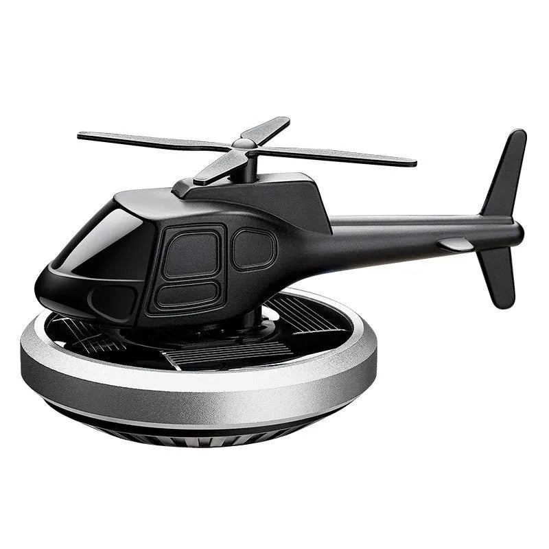 Silver solar-powered metal helicopter car air freshener ornament with rotating blades on a dashboard.