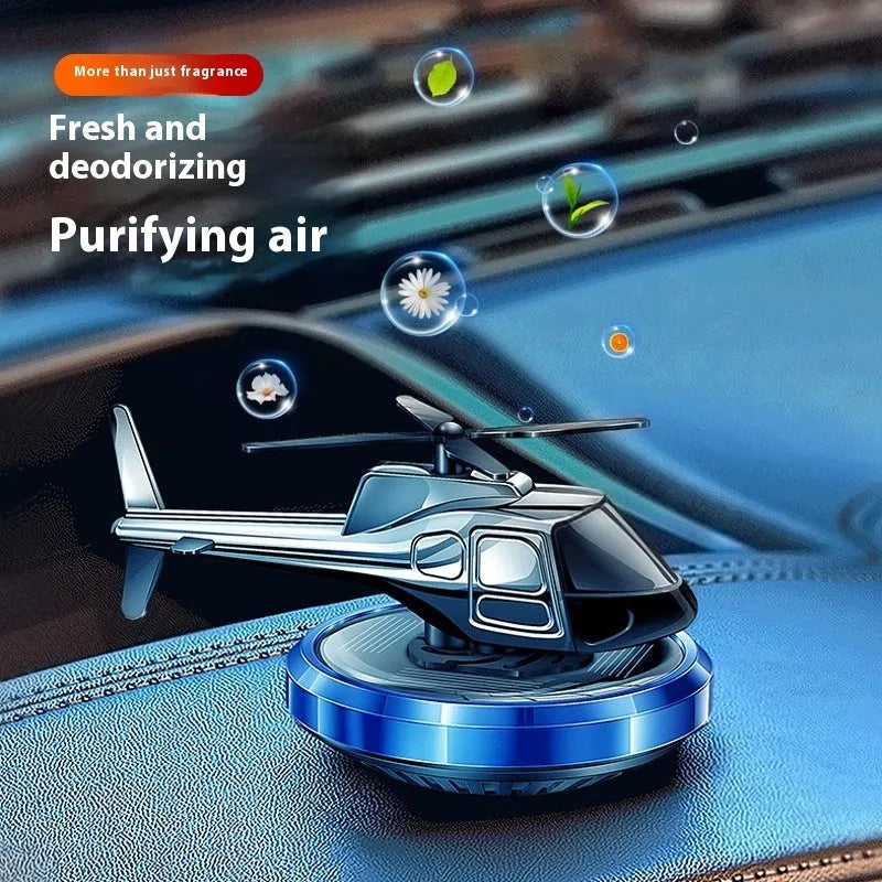 Silver solar-powered metal helicopter car air freshener ornament with rotating blades on a dashboard.