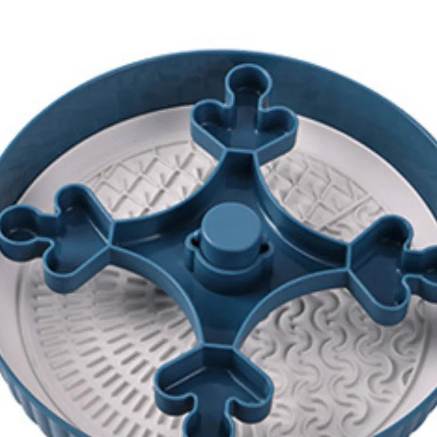 A grey plastic rotating pet bowl with a textured blue silicone slow-feeding mat attached, showing a windmill pattern.