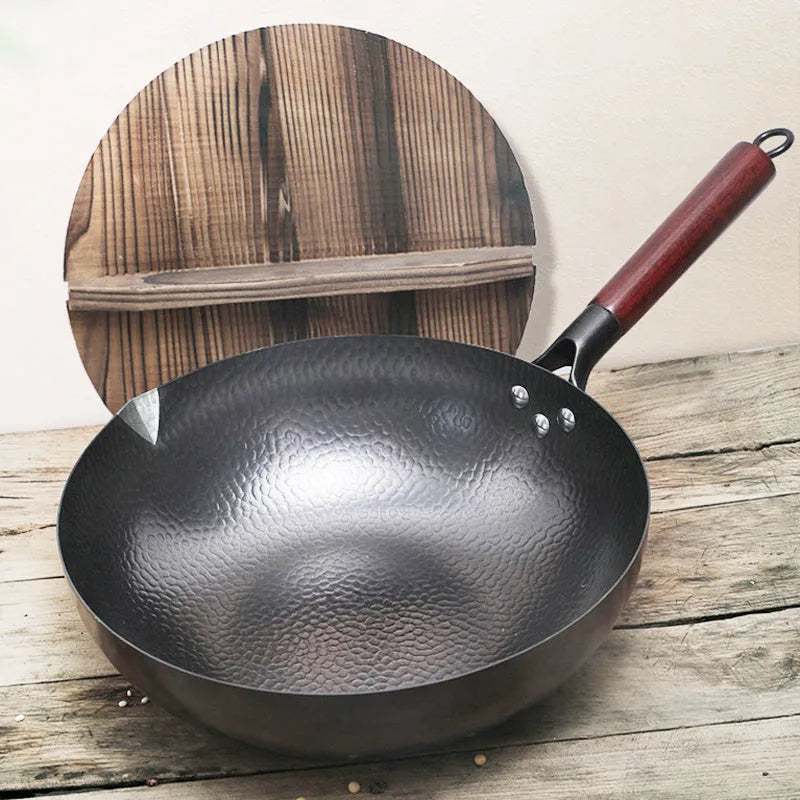 Traditional black iron wok pan with a wooden handle on a hob.