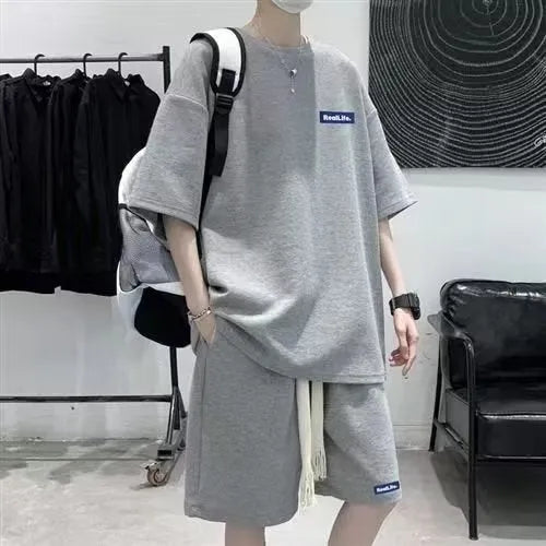 Man wearing a waffle-textured grey short sleeve top and matching shorts from a leisure sports suit set.