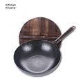 Traditional black iron wok pan with a wooden handle on a hob.