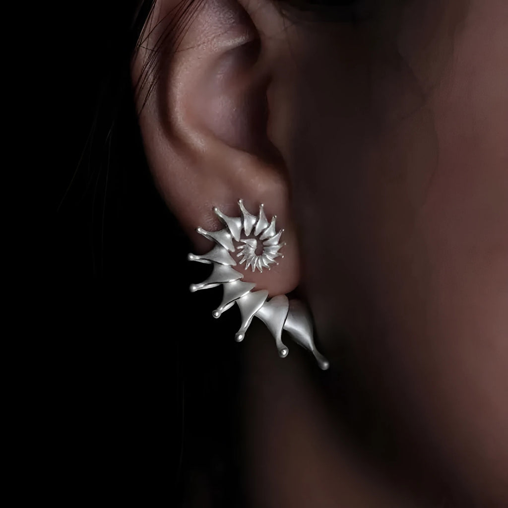Close-up of a pair of matte-finish, three-dimensional conch shell stud earrings.