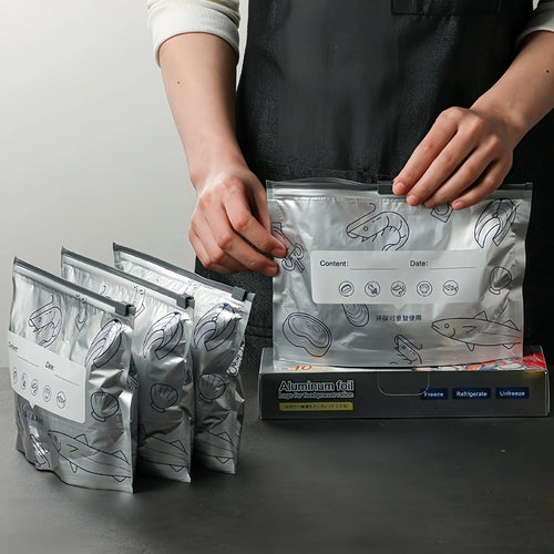 Set of aluminium foil sealed food storage bags and boxes in three different sizes on a kitchen counter.