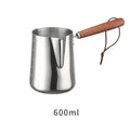Stainless steel milk jug with measurement scale and wooden handle on a counter.