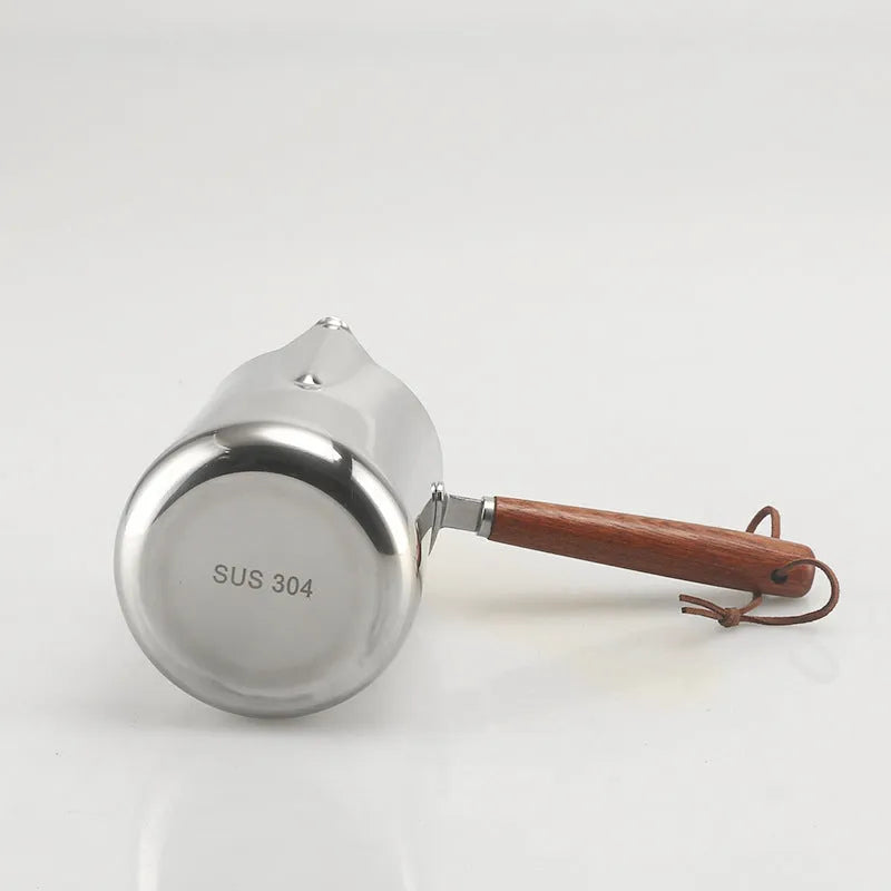 Stainless steel milk jug with measurement scale and wooden handle on a counter.