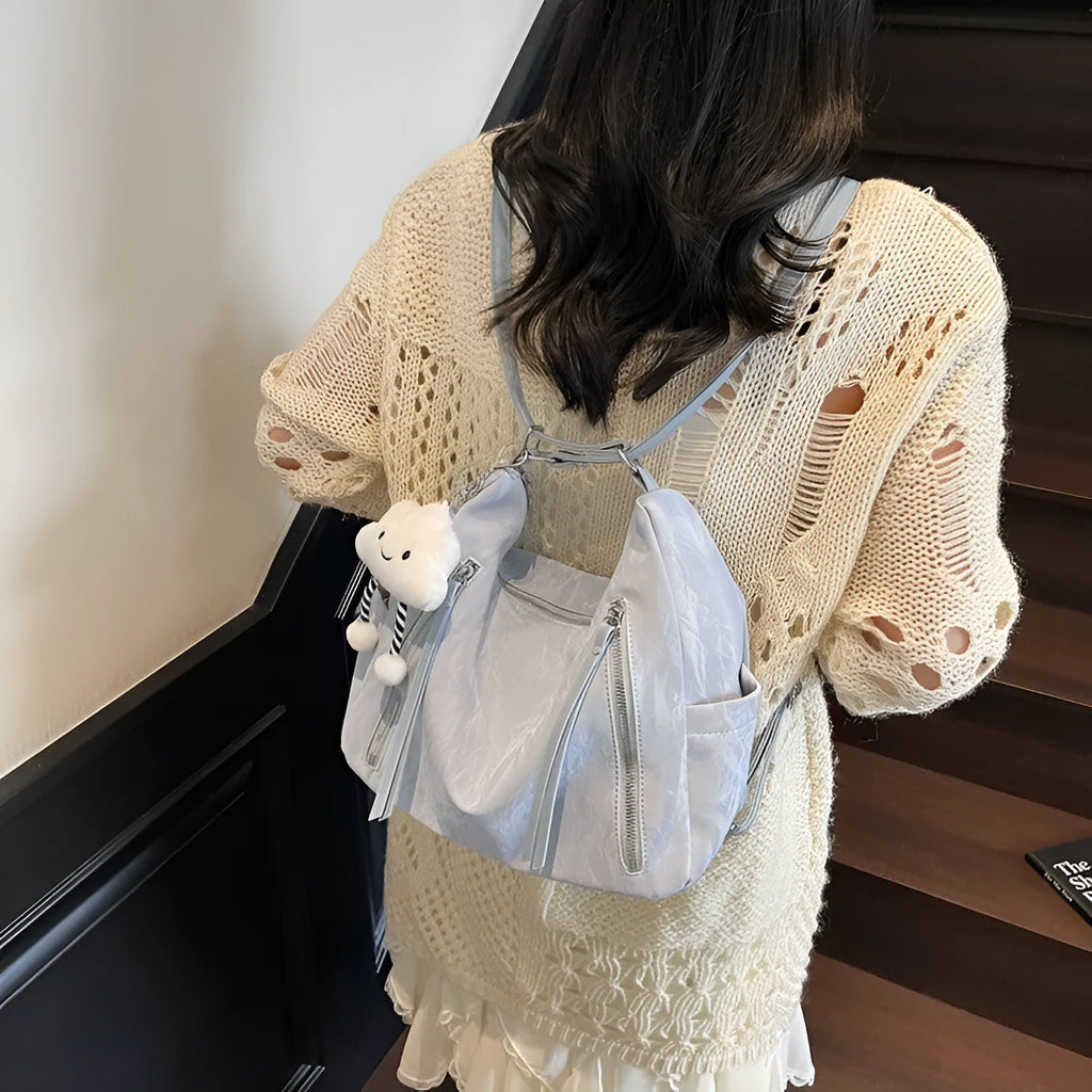 Women's fashion backpack in soft PU leather, shown in black, milky white, silver, and blue colour options with a pendant.