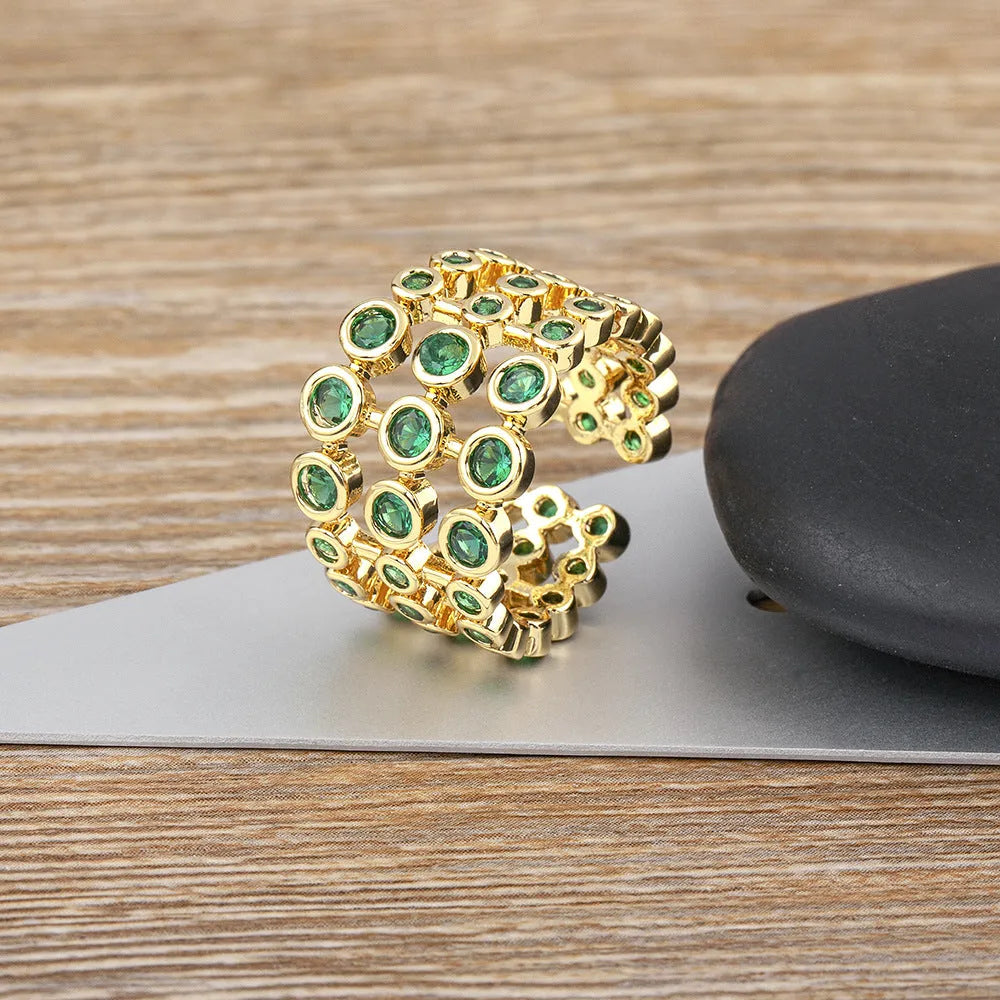 Gold-coloured exaggerated wide band ring with three-layer design and full green zircon stone setting.