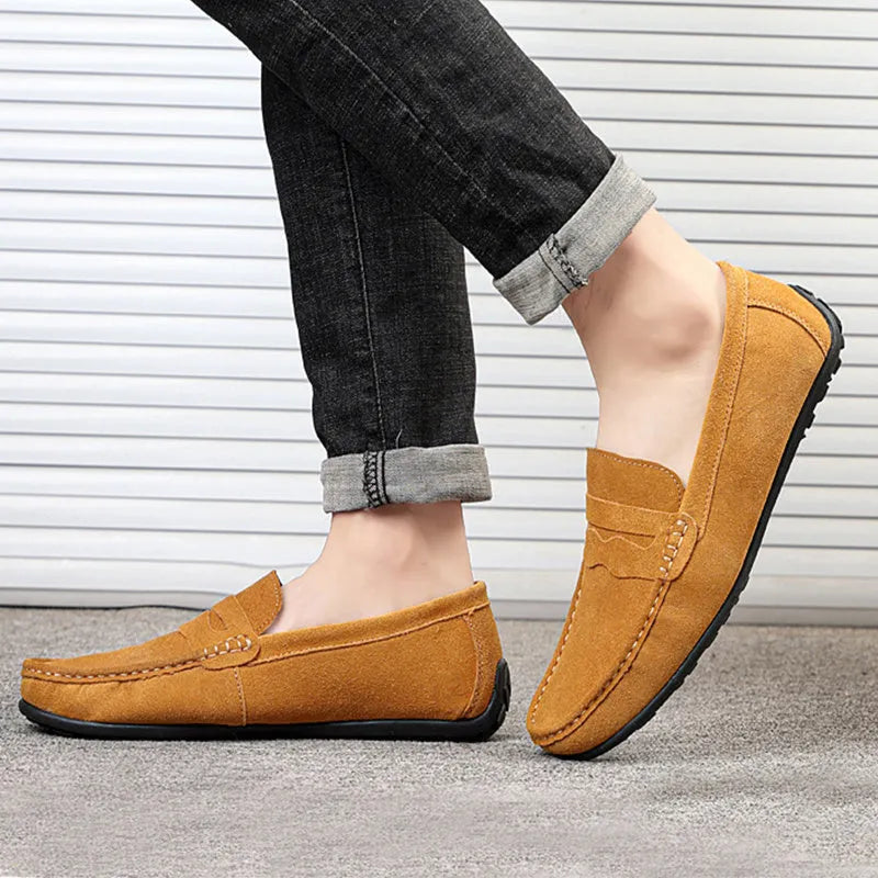 Men's solid colour suede loafers with a round toe and flat rubber sole on a neutral background.