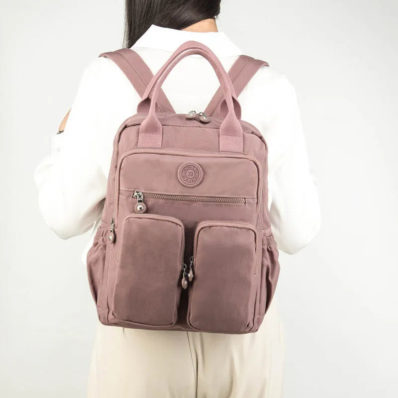 Women's large waterproof nylon travel backpack in lotus root purple showing internal laptop and camera compartments.