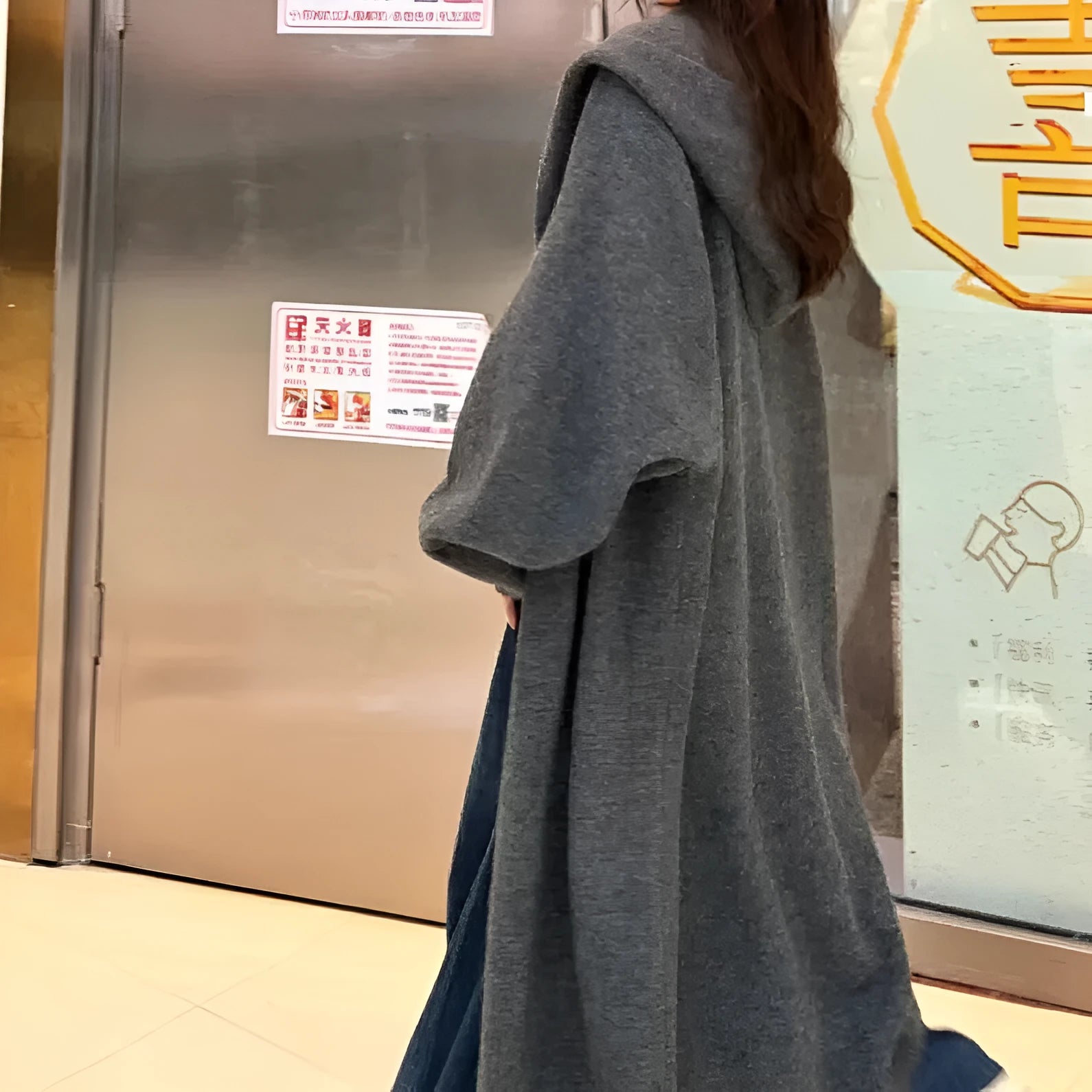 Women's long hooded knitted cardigan in oatmeal colour, showing below-knee length and loose fit.