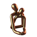 Modern couple resin statue in milky white or gold on a wooden surface.