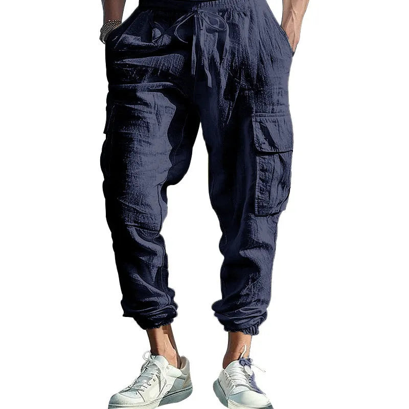 Man wearing loose-fit linen trousers with ankle-tied cuffs and a multi-pocket tether detail.