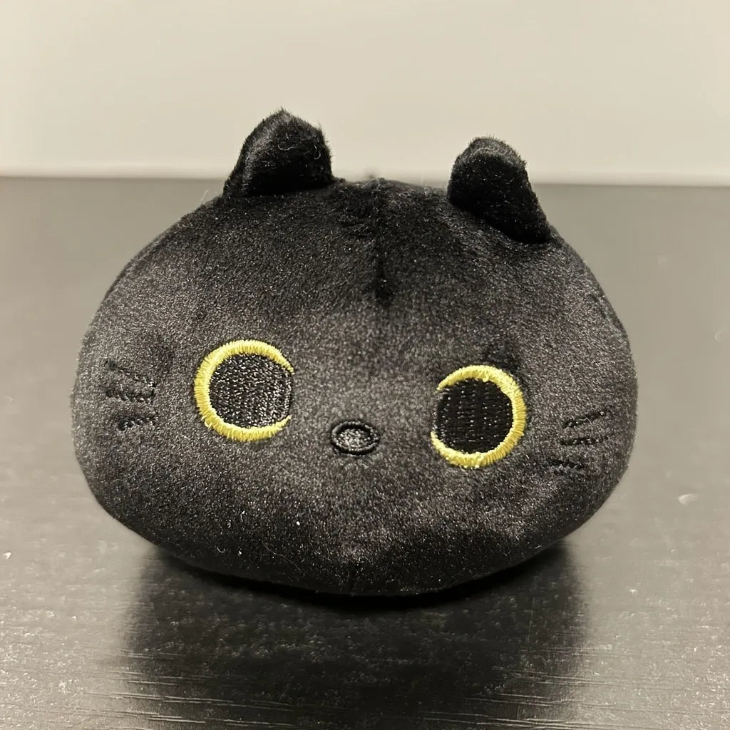 Fluffy black cat stuffed toy with embroidered eyes and whiskers on a grey background.