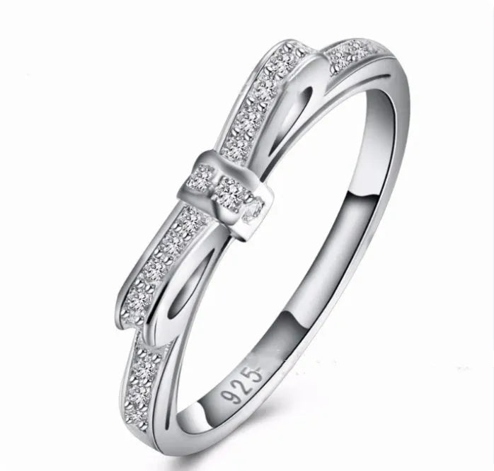 Silver colour bow-shaped ring with rhinestone and zircon crystal decoration on a finger.