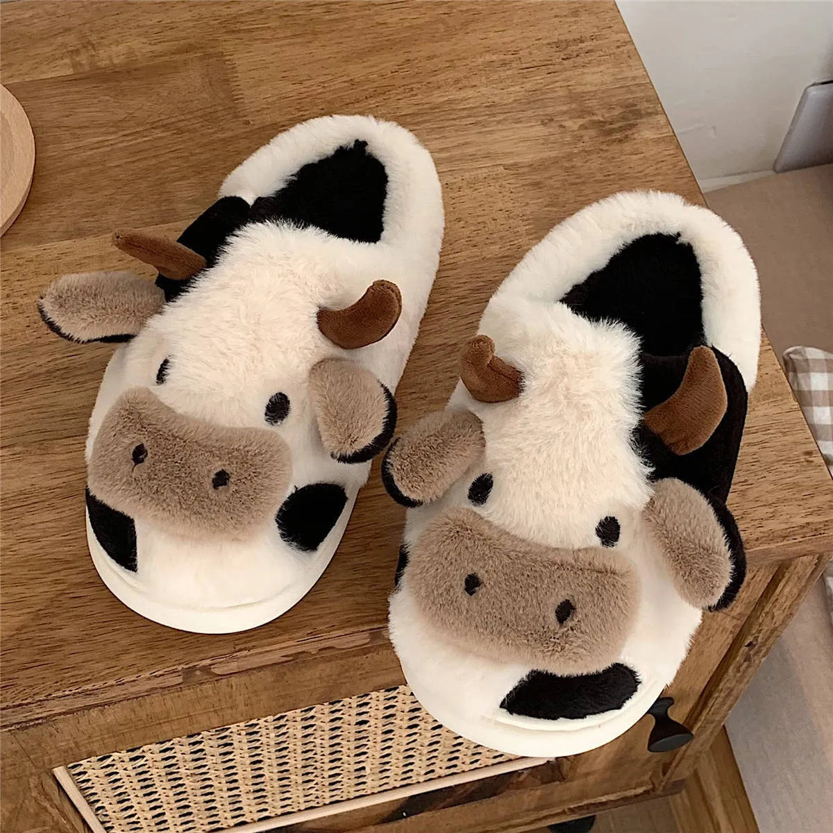 White cow-patterned plush slippers for women with a non-slip textured sole on a wooden floor