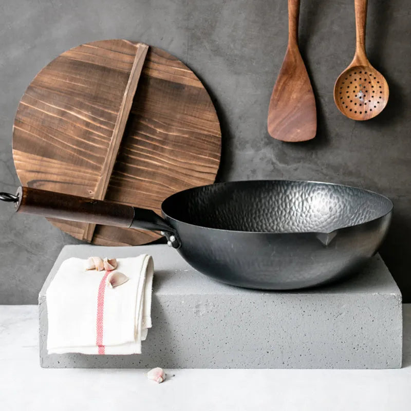 Traditional black iron wok pan with a wooden handle on a hob.