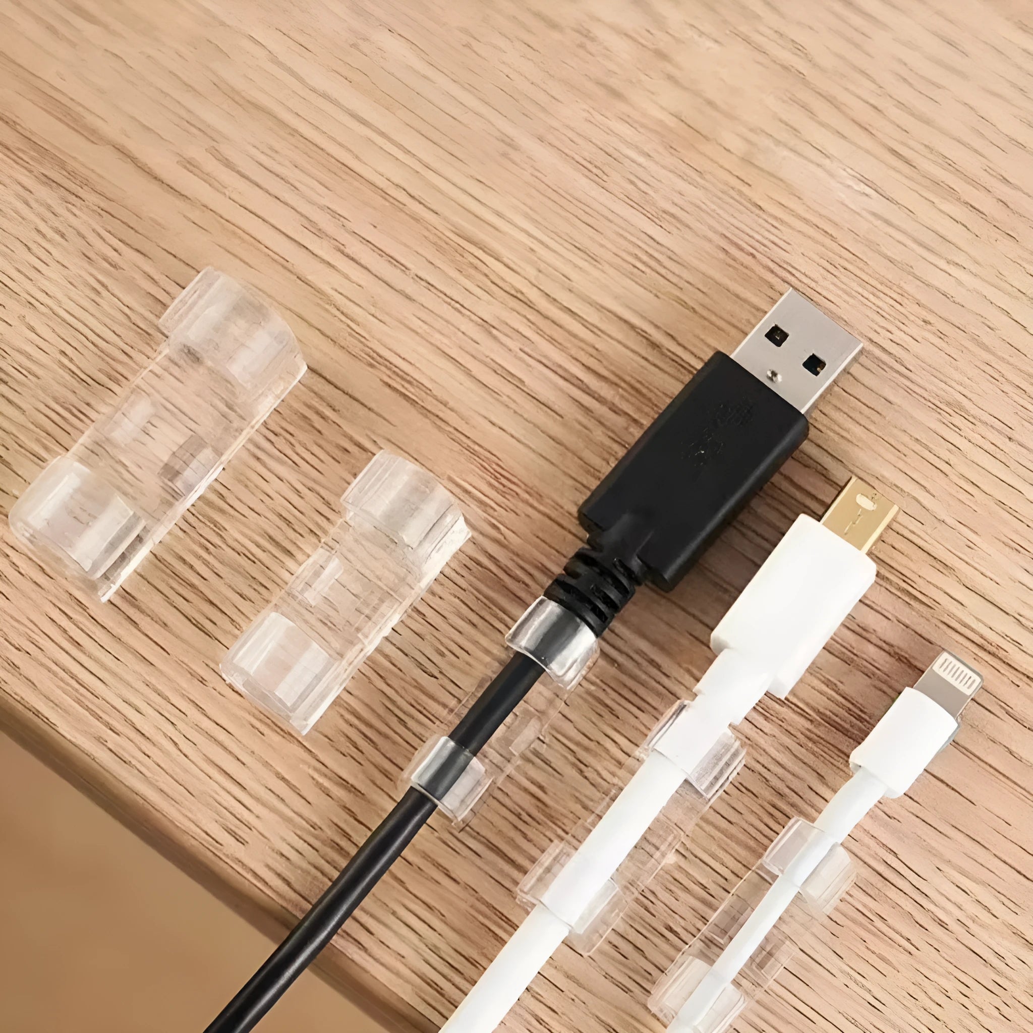 Transparent plastic self-adhesive cable management clips in four sizes on a white background.