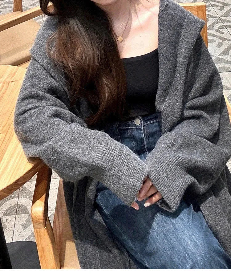Women's long hooded knitted cardigan in oatmeal colour, showing below-knee length and loose fit.