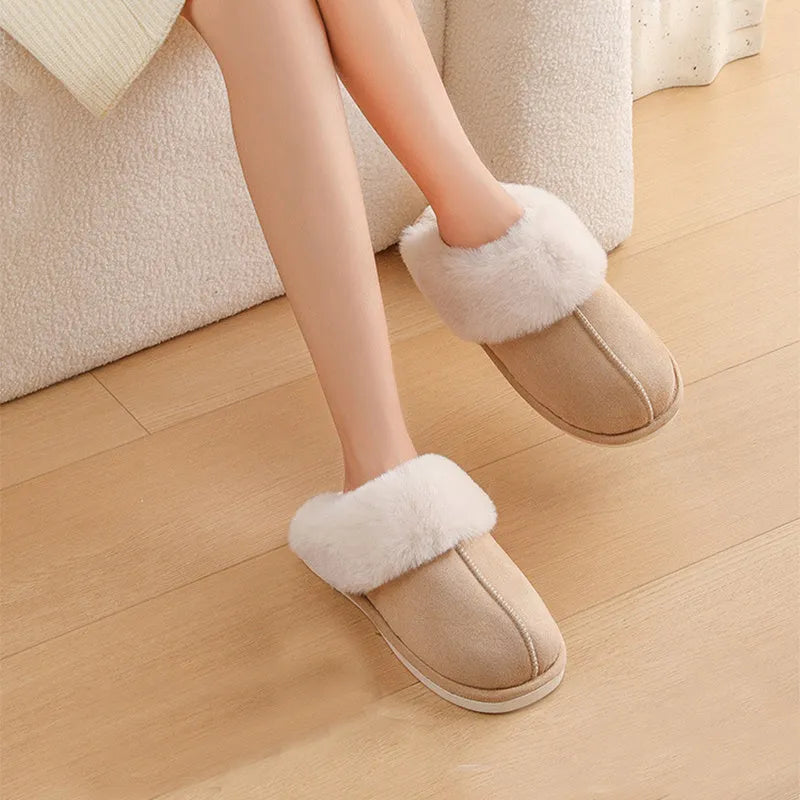 Women's brown plush winter slippers with round toe and flat heel on a wooden floor.