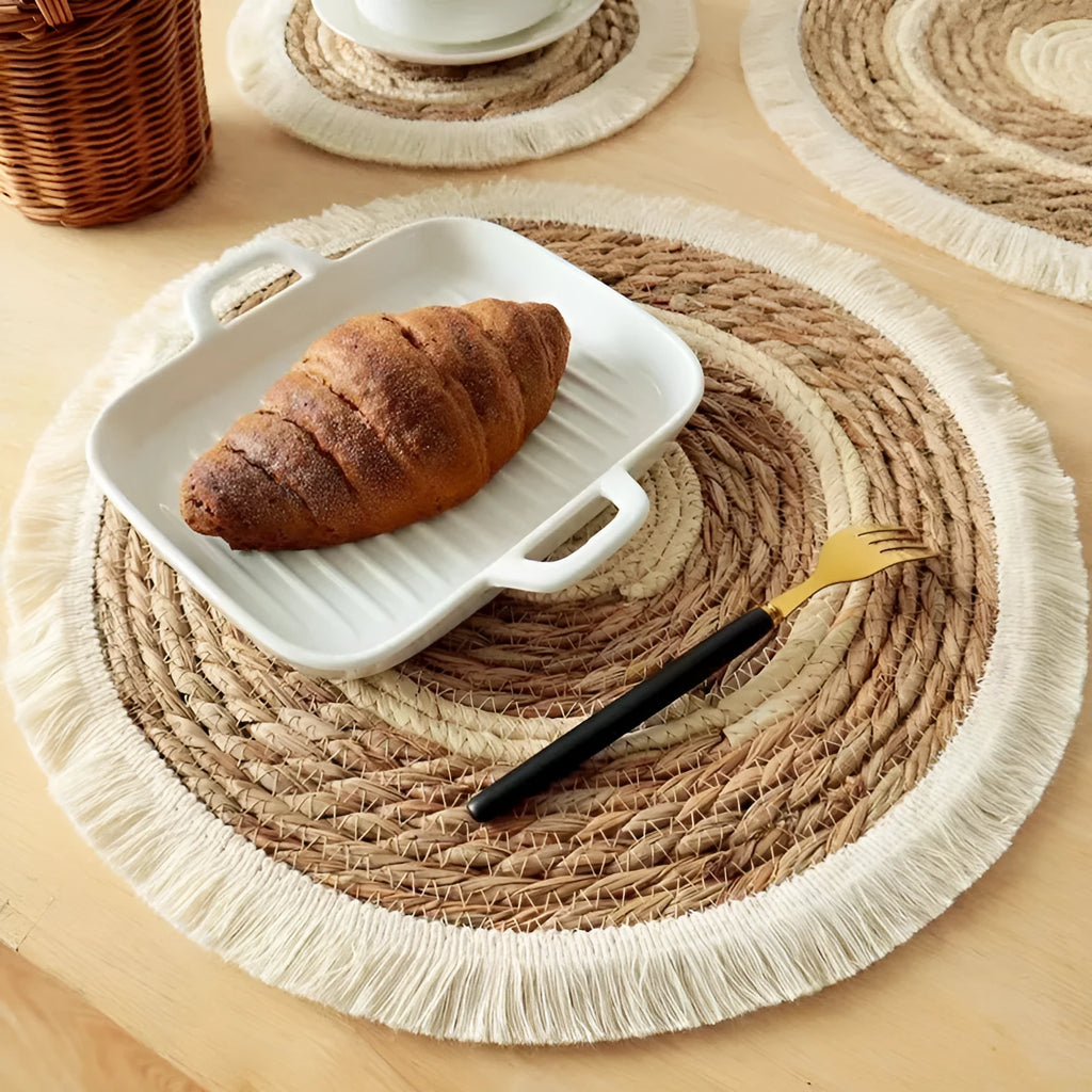 A round natural papyrus straw placemat with decorative tassels, shown in a solid colour.