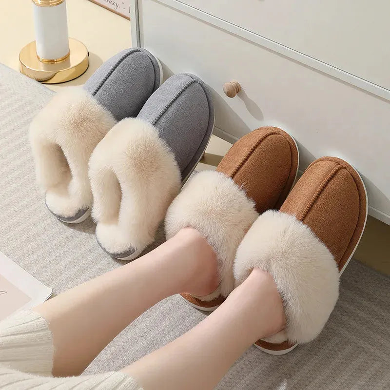 Women's brown plush winter slippers with round toe and flat heel on a wooden floor.