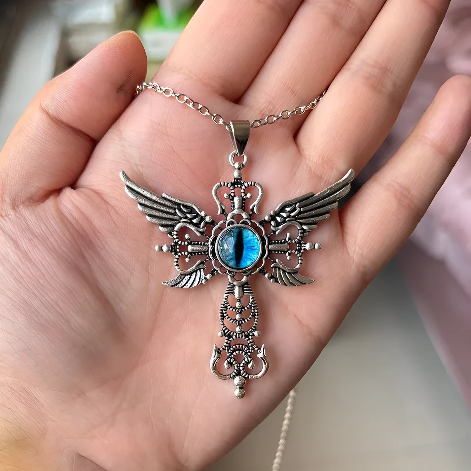Close-up of a devil wings and cross geometric alloy pendant necklace on a chain.