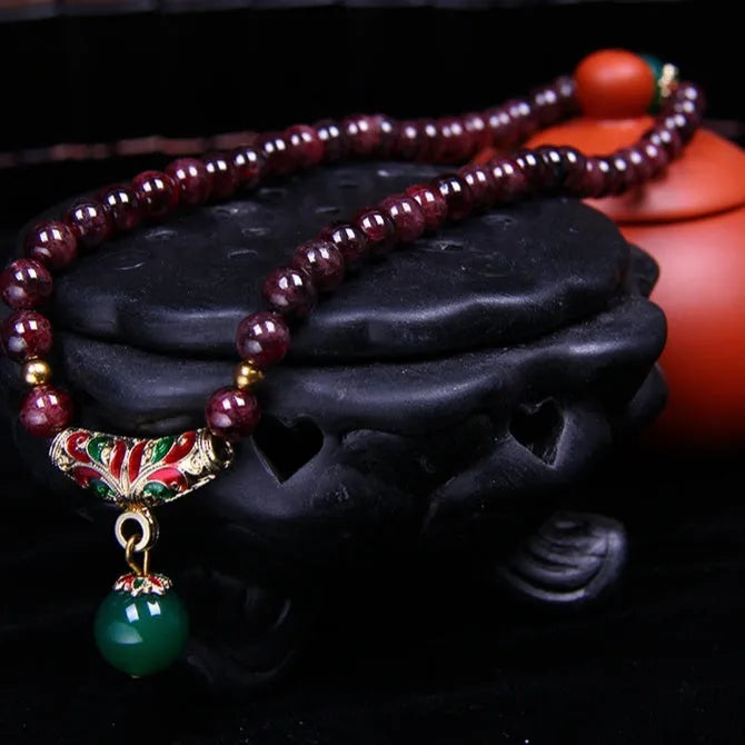 Close-up of a natural deep red garnet bead bracelet with a golden toad charm and double ring clasp.