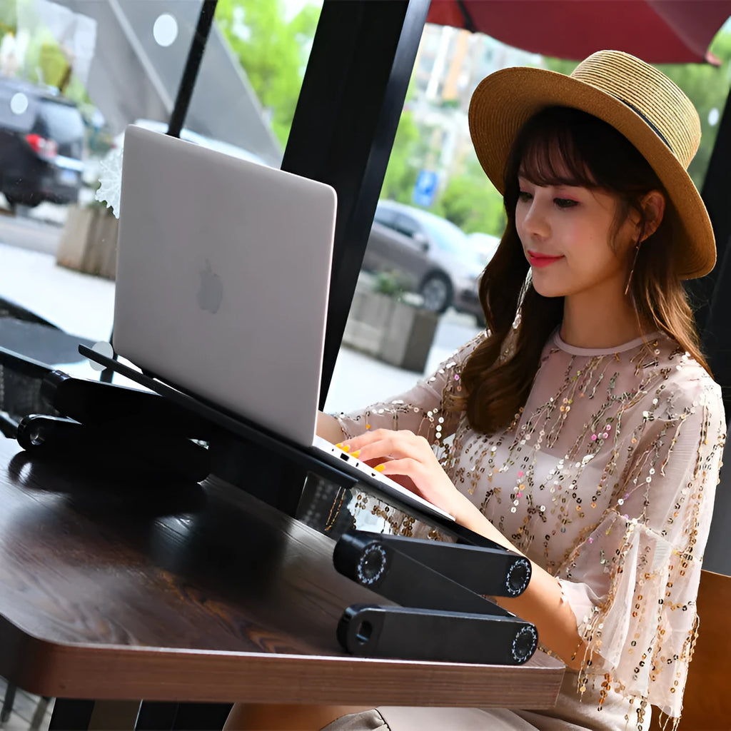 Red folding metal bed table with laptop and cooling fan hole on a wooden floor.