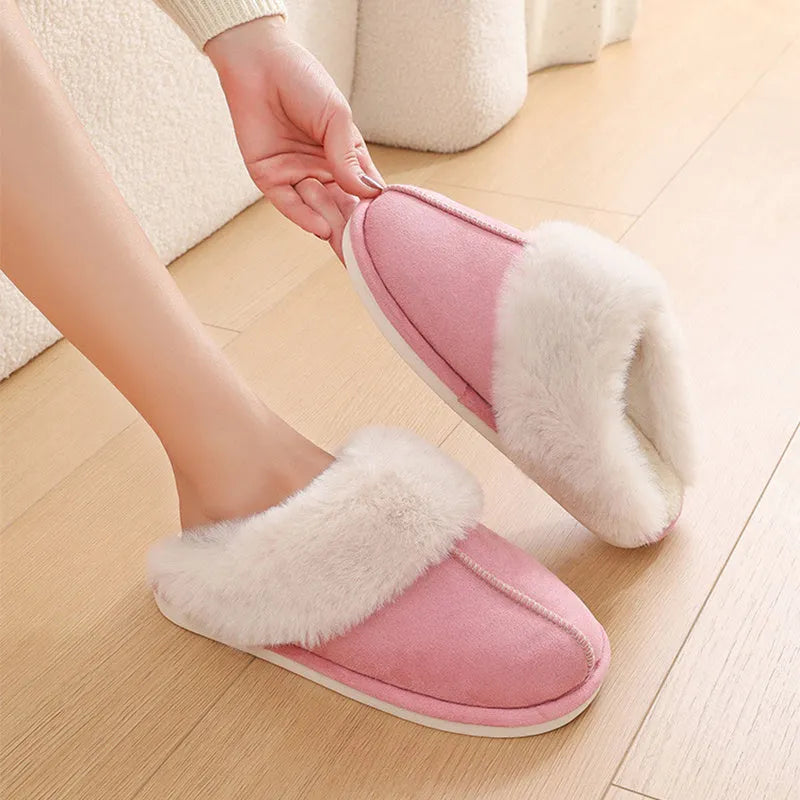 Women's brown plush winter slippers with round toe and flat heel on a wooden floor.
