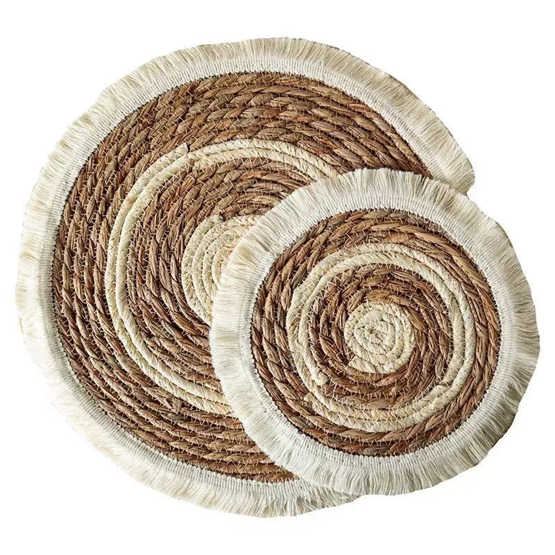 A round natural papyrus straw placemat with decorative tassels, shown in a solid colour.