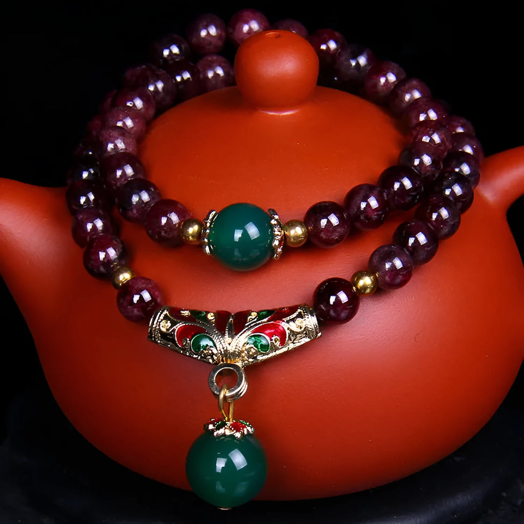 Close-up of a natural deep red garnet bead bracelet with a golden toad charm and double ring clasp.
