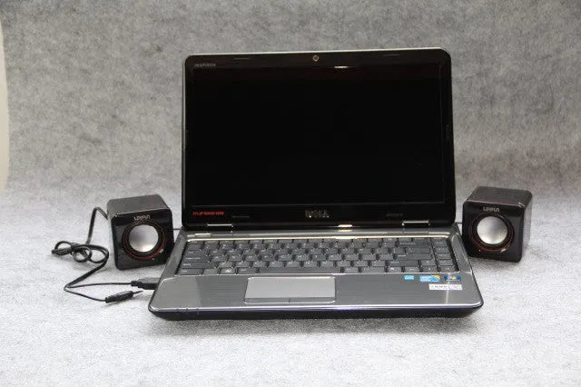 Small black square USB computer speaker on a desk next to a laptop.