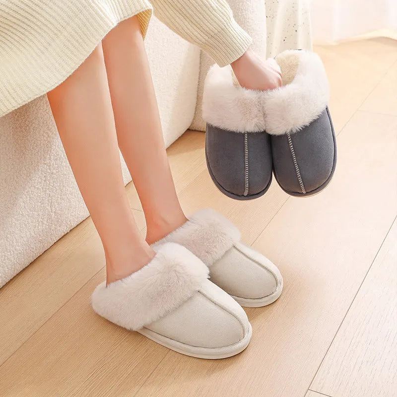 Women's brown plush winter slippers with round toe and flat heel on a wooden floor.