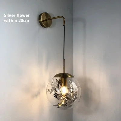 Small modern glass wall lamp in golden flower or silver flower finish for bedside lighting.