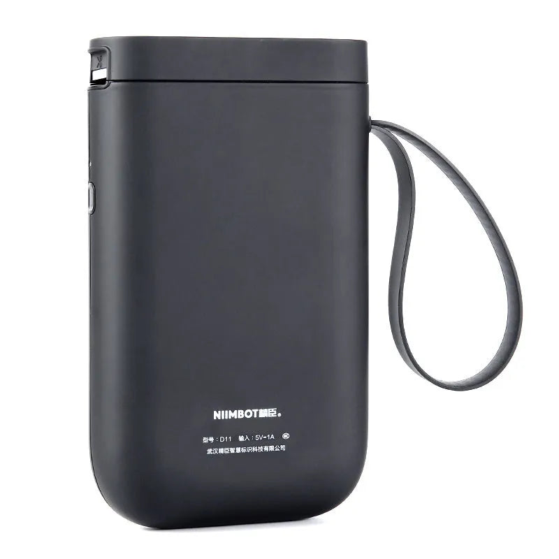 D11 compact white Bluetooth thermal label printer with USB cable and roll of label paper on a desk.