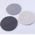 Set of three round grey cotton cord coaster placemats on a wooden table