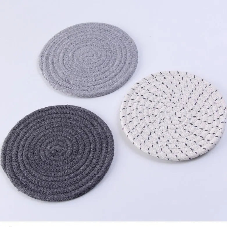 Set of three round grey cotton cord coaster placemats on a wooden table