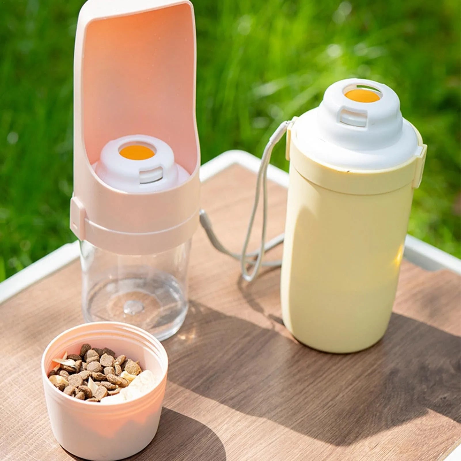Grey folding travel dog water bottle with attached lanyard and separate food container, shown next to a backpack.