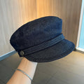 Dark blue denim newsboy cap with an adjustable strap, shown on a model