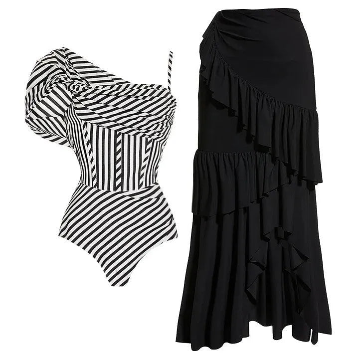 A woman wearing a ruffled striped one-piece swimsuit with a matching black skirt on a beach.