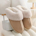 Women's brown plush winter slippers with round toe and flat heel on a wooden floor.