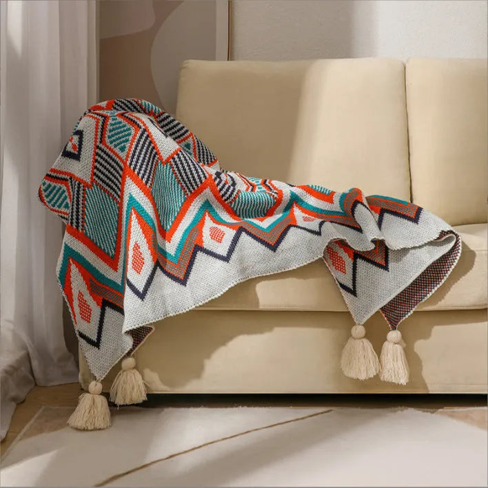 Bohemian style acrylic blanket with tassel fringe on a sofa, shown in a geometric print colour.
