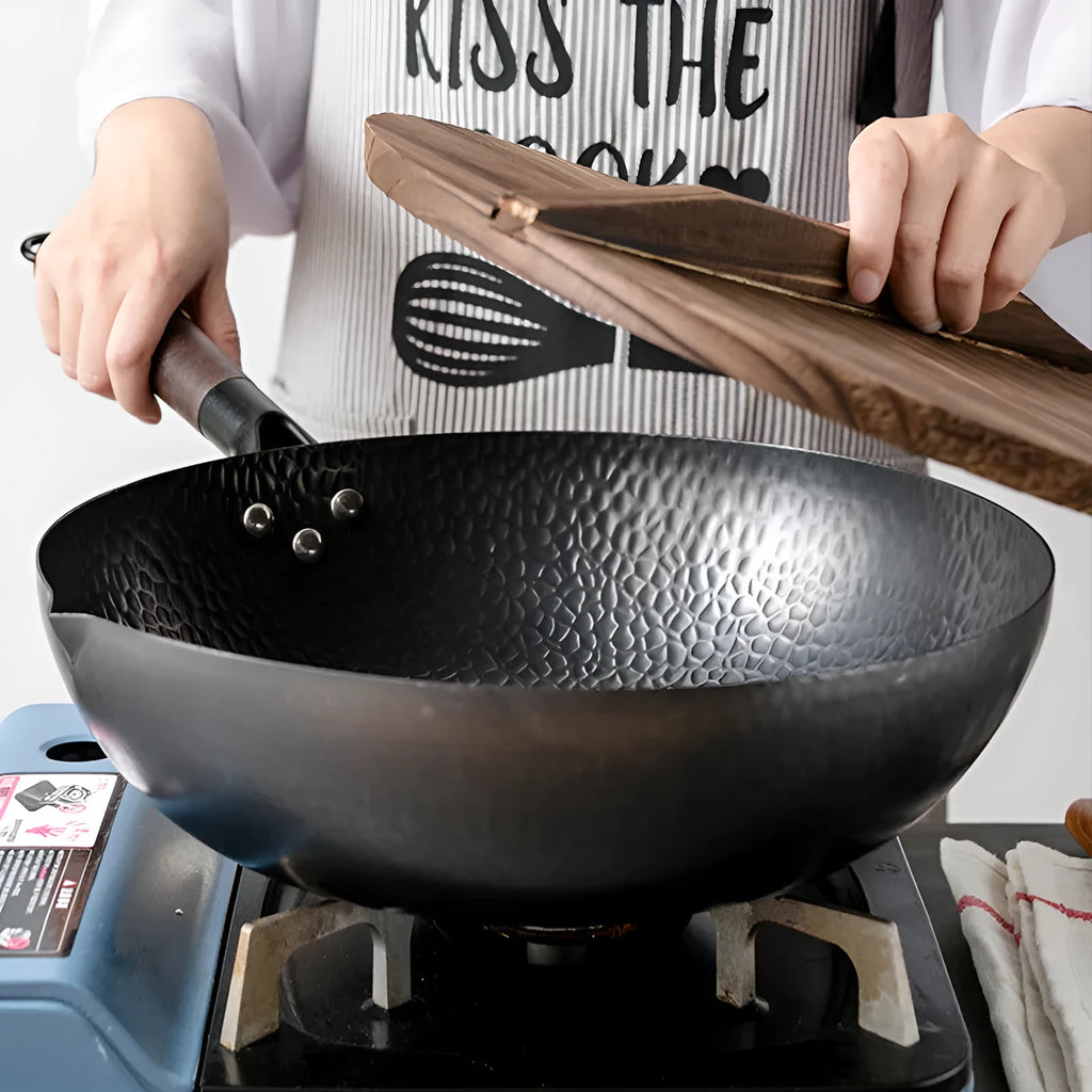 Traditional black iron wok pan with a wooden handle on a hob.