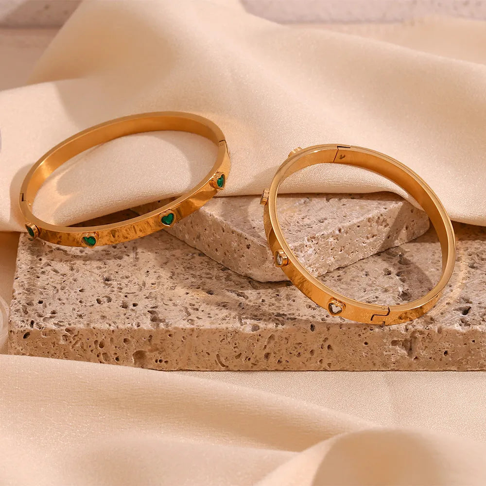 A stainless steel bracelet with a small micro-inlaid peach heart charm, shown in a golden electroplated finish.